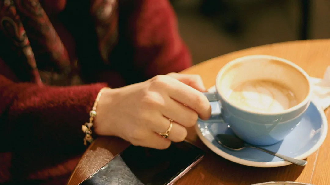 Cliente tomando café com o celular na mesa de uma cafeteria