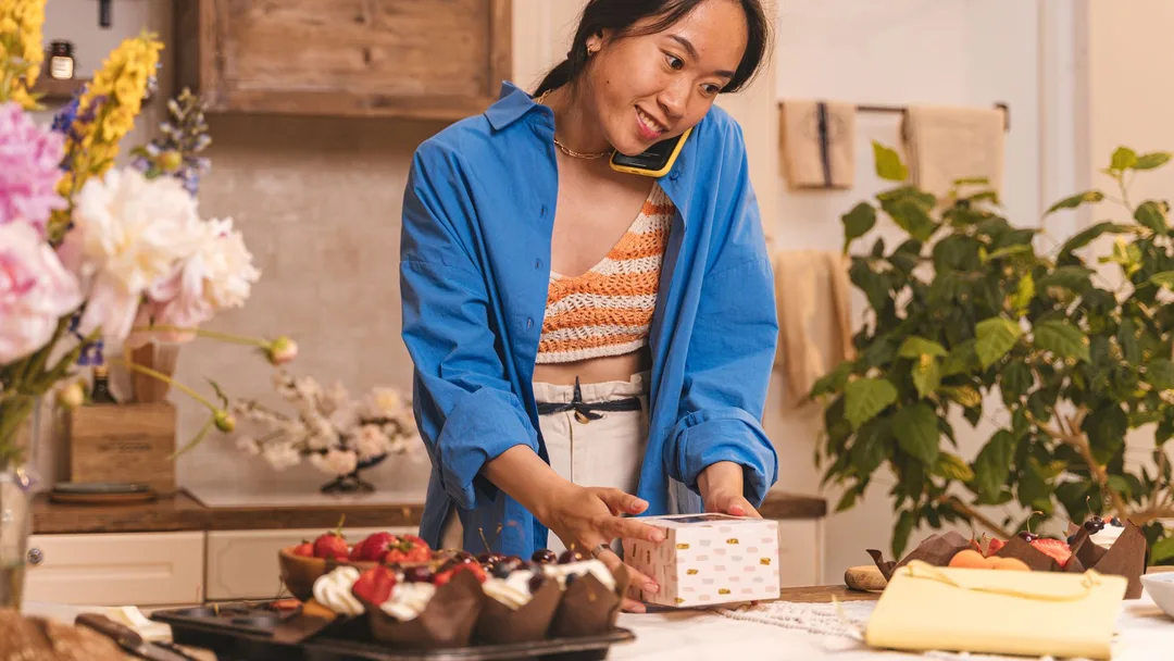 Dona de confeitaria sorrindo ao celular no balcão